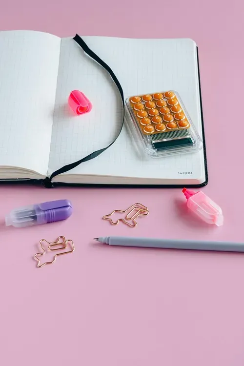 bookkeeping ready Stationery items including a notebook, colourful highlighters, paperclips, and a grey pen on a pink background, symbolizing organisation and productivity for bookkeeping and financial clarity.